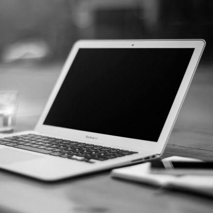 open mac book, a glass of water and a notebook, placed on a table, indicating 'work mode'